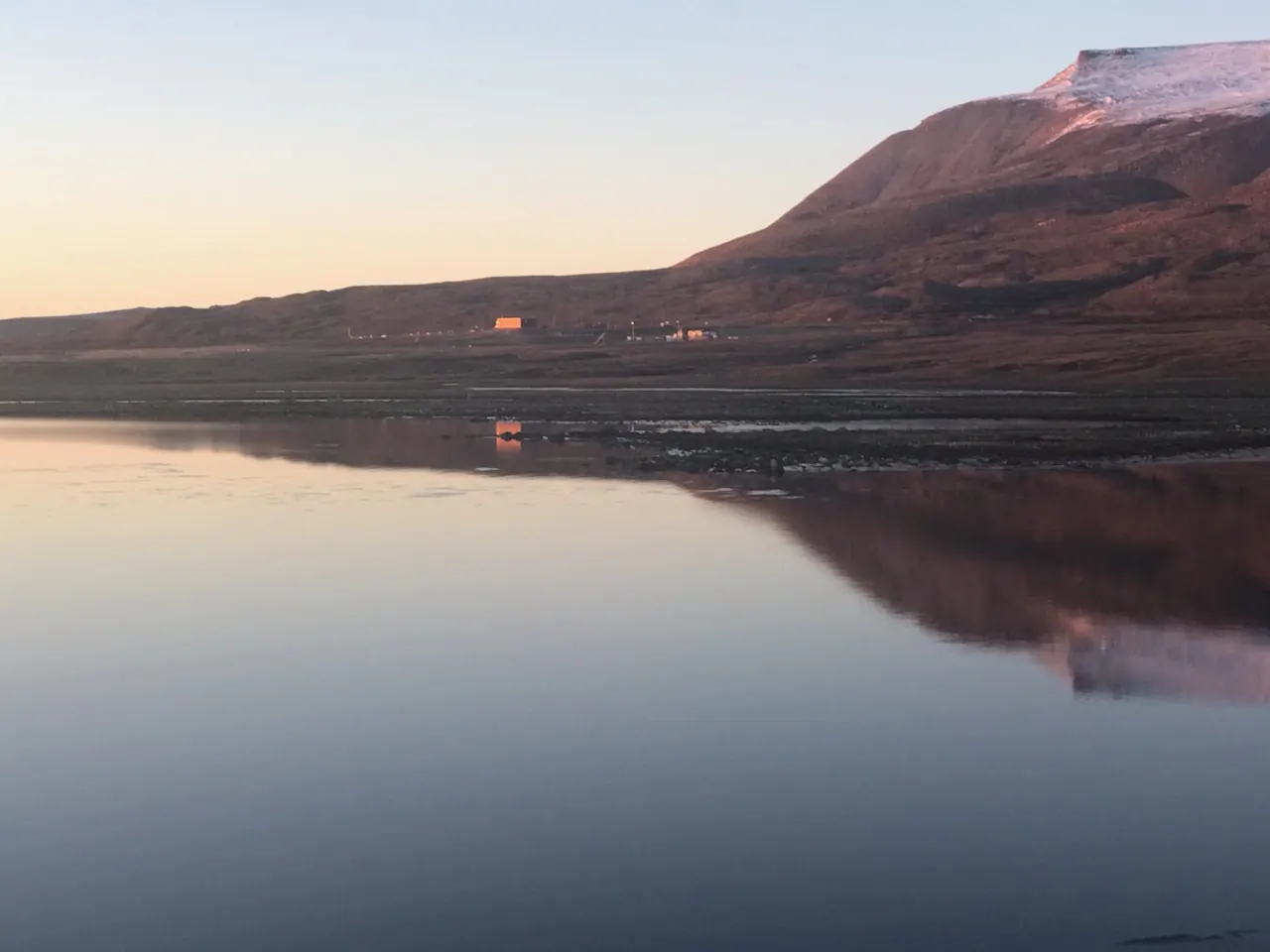 A northern hillside lit pink by the low sun, reflected in still water